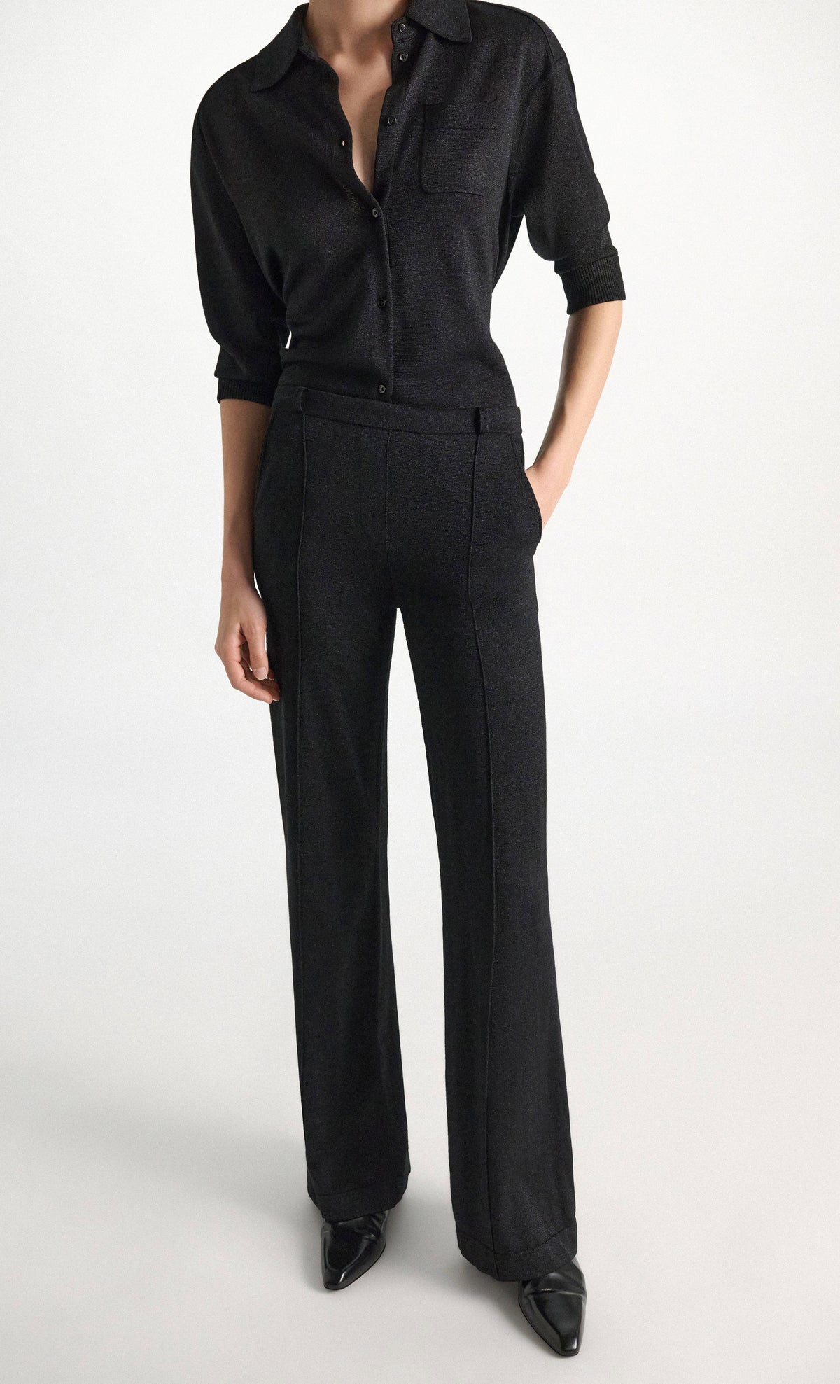 A person wearing a shimmering Merino-Lurex button-down shirt with elbow-length sleeves and matching high-waisted flared Shimmering Merino Trouser pants by Dorothee Schumacher.