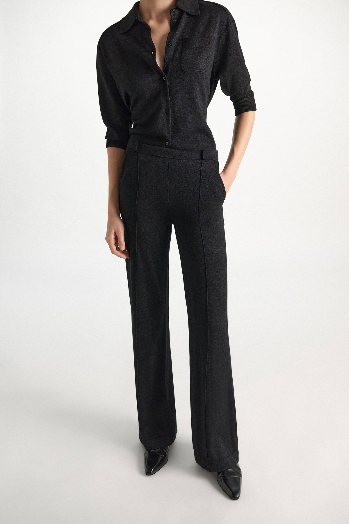 A person wearing a shimmering Merino-Lurex Shimmering Merino Cardigan with elbow-length sleeves and matching wide-leg trousers.