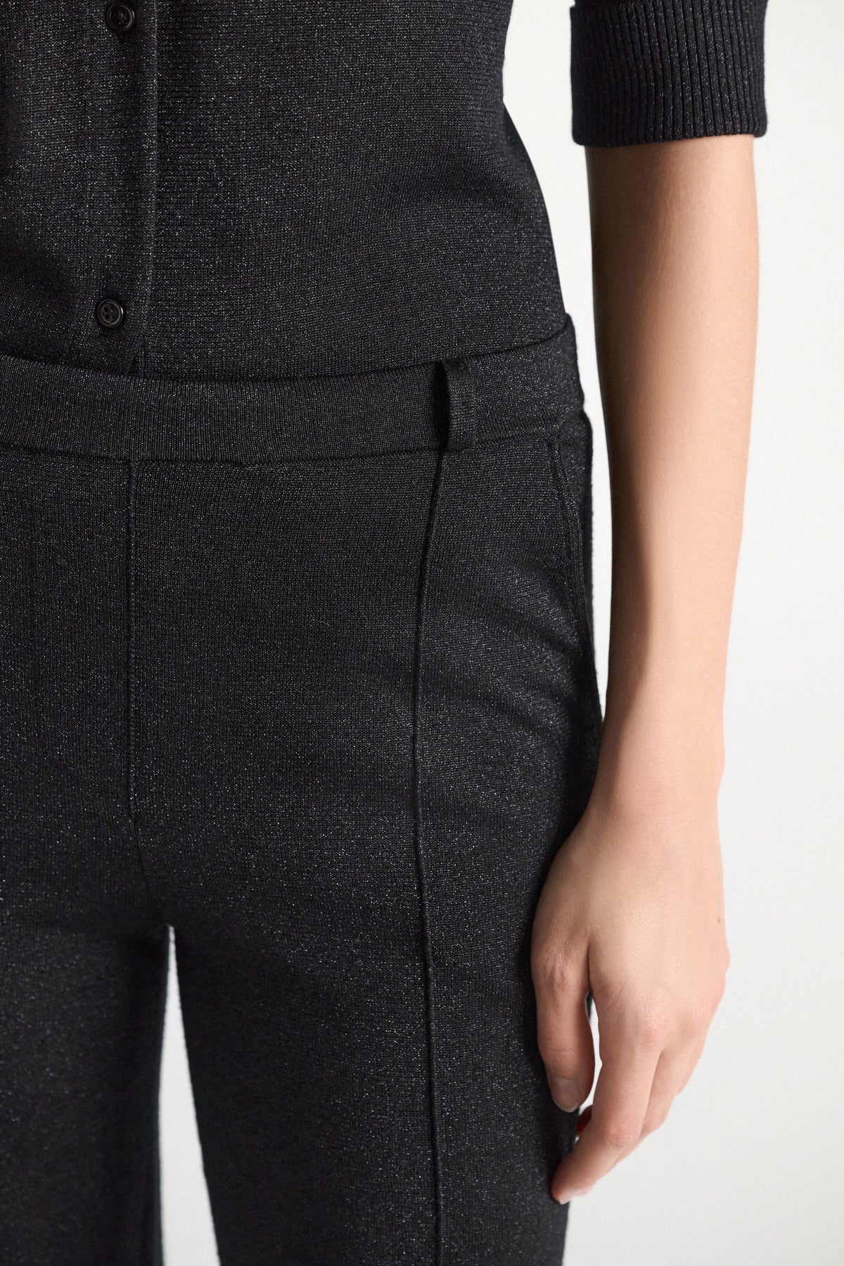Close-up of a person wearing a shimmering Merino-Lurex set by Dorothee Schumacher, featuring Shimmering Merino Trouser flared pants with a front seam paired with a matching button-down top.