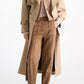 A person wearing a tan trench coat, a neutral-toned quilted knit cardigan, and Dorothee Schumacher Everyday Cool Pants in brown with white side stripes and side slits at the hem.