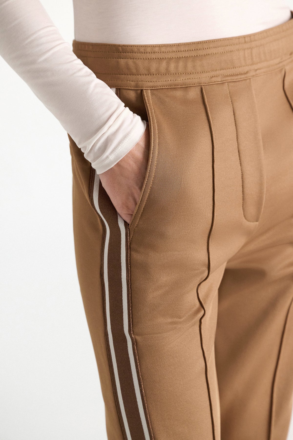 Close-up of tan quilted knit Everyday Cool Pant by Dorothee Schumacher, featuring a white and brown stripe down the side and a hand in the pocket.