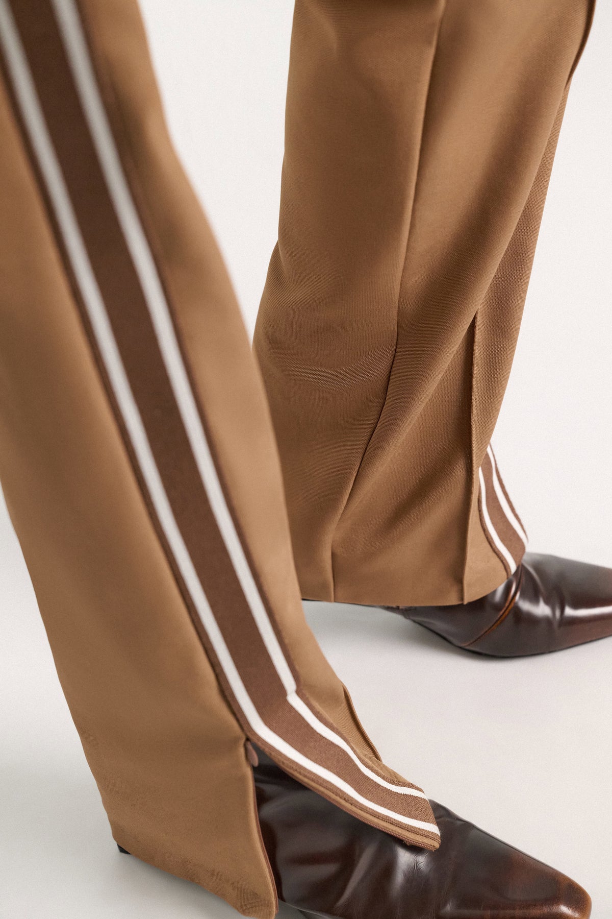 Dorothee Schumacher Everyday Cool Pant in tan quilted knit with side slits and brown and white racing stripes, worn with dark brown leather boots.