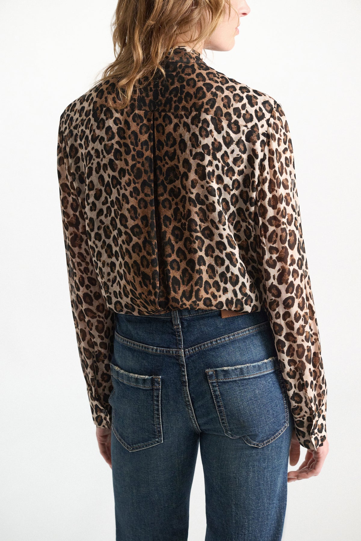 A person seen from behind, wearing a Dorothee Schumacher Wild at Heart Blouse with a high collar tucked into blue jeans.