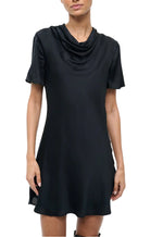 A woman wearing the Staud Iris Silk Dress, a black mini dress with a cowl neck, stands against a white background.