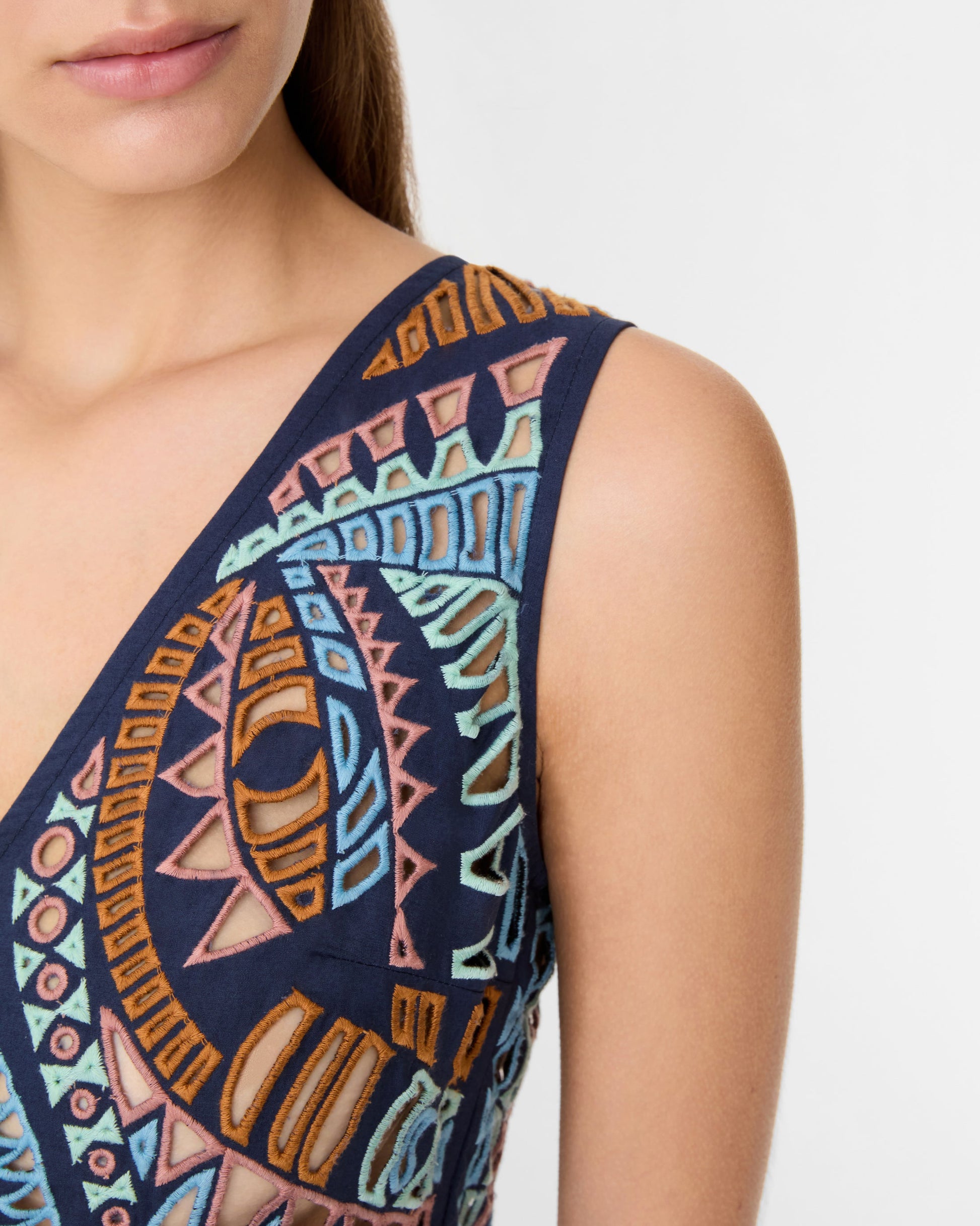 A woman wears the Emporio Sirenuse Vivienne Brise Dress, a sleeveless design featuring multicolored geometric patterns, a deep V-neckline, and delicate Brisé Cutwork.