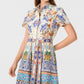 A woman wears the Emporio Sirenuse Giselle Chimera Dress, a short-sleeved style featuring a vibrant, intricate print inspired by Indonesian textiles and belted at the waist.