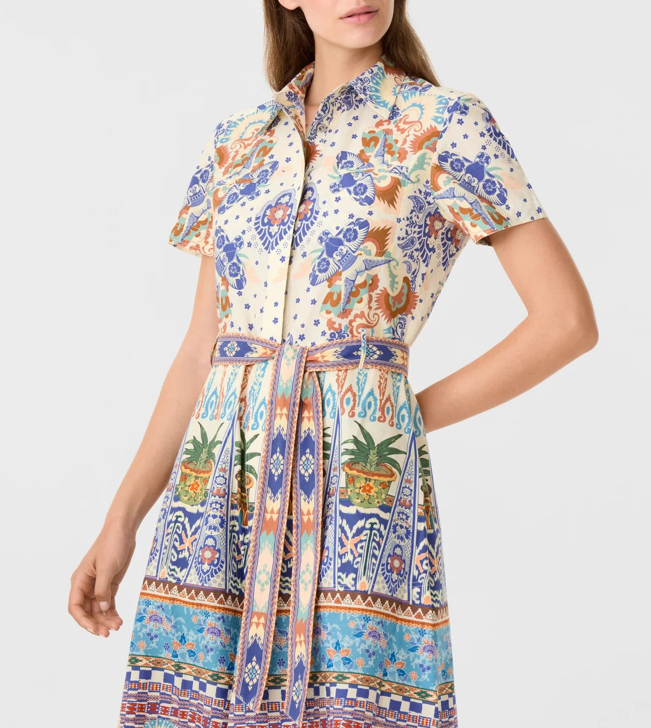 A woman wears the Emporio Sirenuse Giselle Chimera Dress, a short-sleeved style featuring a vibrant, intricate print inspired by Indonesian textiles and belted at the waist.