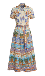 The Emporio Sirenuse Giselle Chimera Dress is a short-sleeve, button-up style with a belted waist, featuring a vibrant print inspired by Indonesian textiles in blue, orange, and green with florals, palms, and geometric motifs.