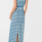 A woman wearing the Emporio Sirenuse Kimi Ikat Stripes Dress, a sleeveless blue and white handwoven maxi with a back slit, stands facing away from the camera.