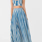 A woman wears the Emporio Sirenuse Flaminia Ikat Stripes Skirt with a matching blue and white crop top and sandals, her hands in her pockets.