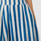 Close-up of a person wearing the Emporio Sirenuse Flaminia Ikat Stripes Skirt, crafted from handwoven pleated fabric with vertical blue and white Ikat stripes.