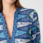 A woman wearing the Emporio Sirenuse Jenna Kites Caftan Dress, showcasing a blue batik-inspired floral and geometric pattern reminiscent of kites; only her lower face and upper torso are visible.