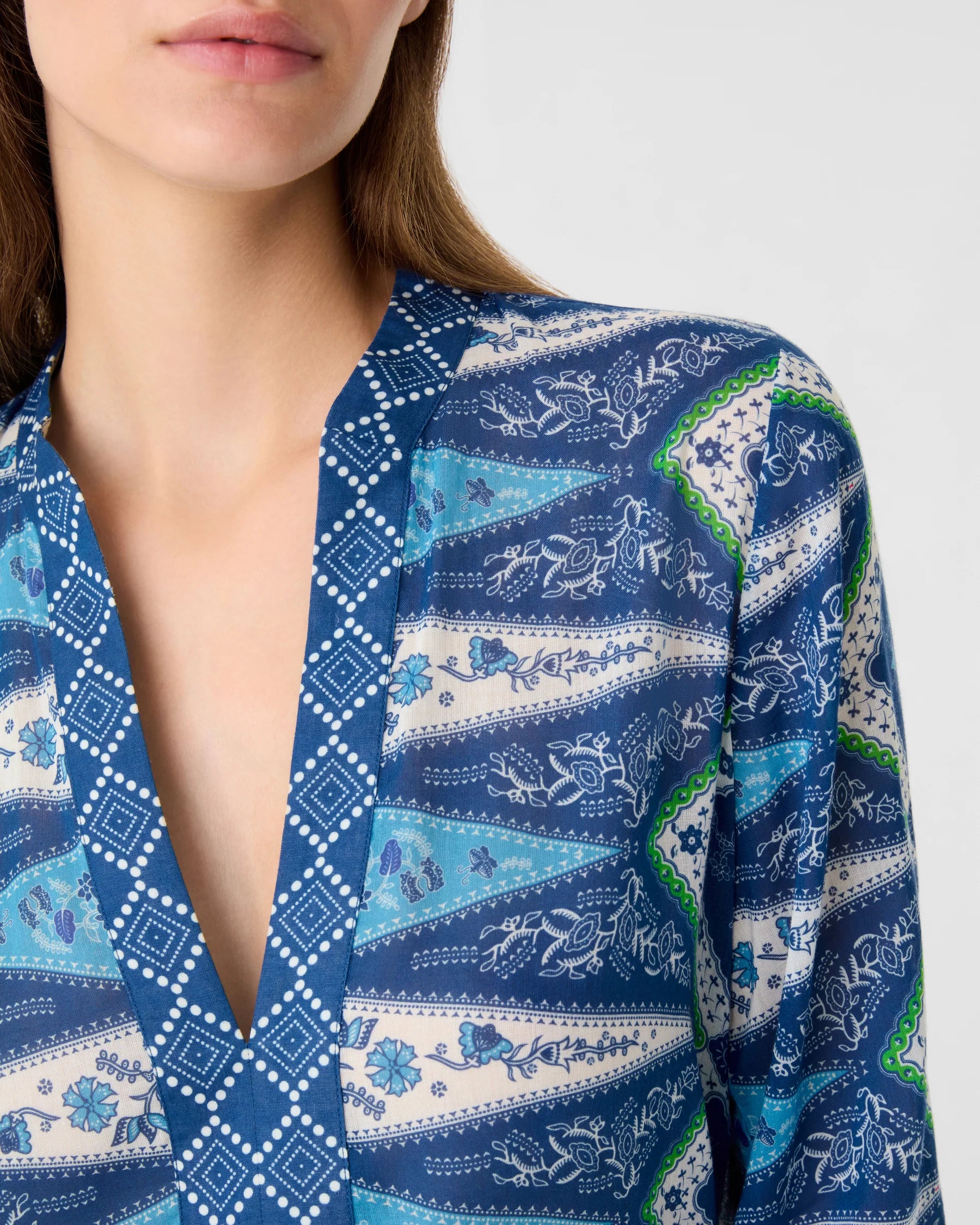 A woman wearing the Emporio Sirenuse Jenna Kites Caftan Dress, showcasing a blue batik-inspired floral and geometric pattern reminiscent of kites; only her lower face and upper torso are visible.