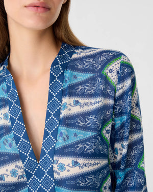 A woman wearing the Emporio Sirenuse Jenna Kites Caftan Dress, showcasing a blue batik-inspired floral and geometric pattern reminiscent of kites; only her lower face and upper torso are visible.