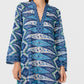 A person wearing the Jenna Kites Caftan Dress by Emporio Sirenuse, a long-sleeved blue dress with a v-neckline, adorned with geometric and batik-inspired floral patterns.