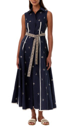 A woman wears the Emporio Sirenuse Miralda Dress with Iris Embroidery, a sleeveless navy cotton poplin dress with white trim, paired with white sandals.