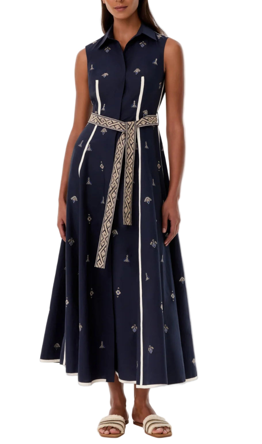 A woman wears the Emporio Sirenuse Miralda Dress with Iris Embroidery, a sleeveless navy cotton poplin dress with white trim, paired with white sandals.