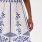 A person models the Emporio Sirenuse Camille Skirt with Iris Embroidery, featuring blue floral and geometric designs on white cotton poplin, shown from waist to mid-thigh against a plain background.