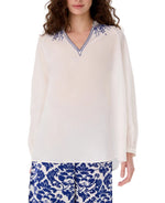 A woman wearing the Emporio Sirenuse Ilizia Blouse with Iris Embroidery and patterned blue-and-white pants.