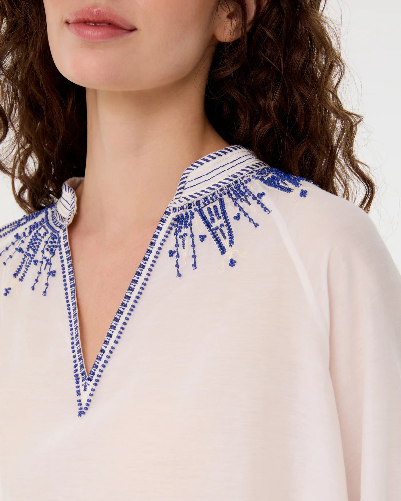 Close-up of a woman wearing the Emporio Sirenuse Ilizia Blouse with Iris Embroidery, featuring a cotton-silk blend, V-shaped neckline, and blue hand-finished embroidery on the collar and shoulders.