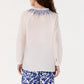 A woman is seen from the back wearing the Emporio Sirenuse Ilizia Blouse with iris embroidery and blue and white patterned pants.