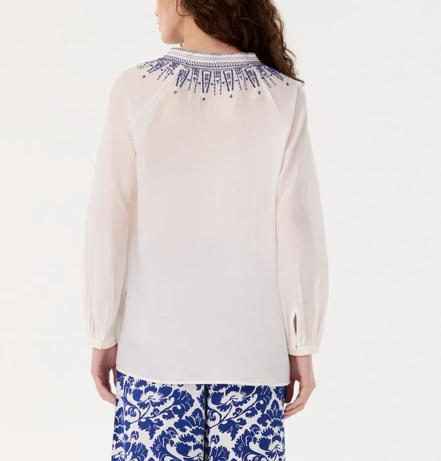 A woman is seen from the back wearing the Emporio Sirenuse Ilizia Blouse with iris embroidery and blue and white patterned pants.
