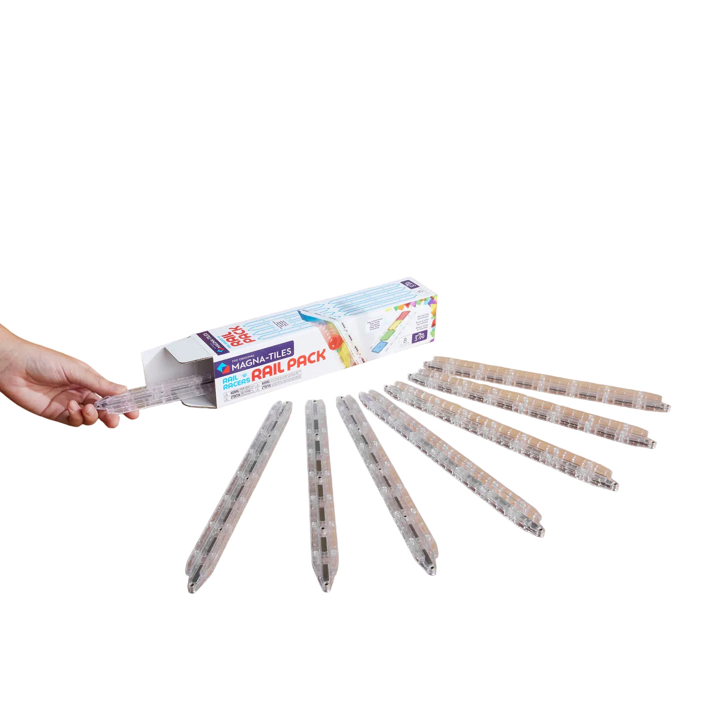 A hand holds a translucent clear rail piece next to an open Magnatiles Rail Racers 8-Piece Rail Pack box, with seven similar rails arranged in a row on a white surface.
