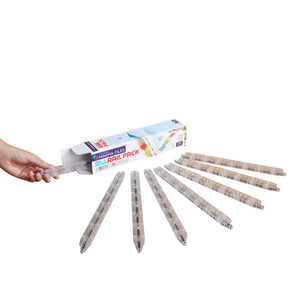 A hand holds a translucent clear rail piece next to an open Magnatiles Rail Racers 8-Piece Rail Pack box, with seven similar rails arranged in a row on a white surface.