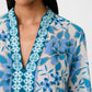 A woman wears the Emporio Sirenuse Jenna Eastern Dream Dress, crafted in soft cotton voile with a blue and white print and geometric embroidery along the neckline.