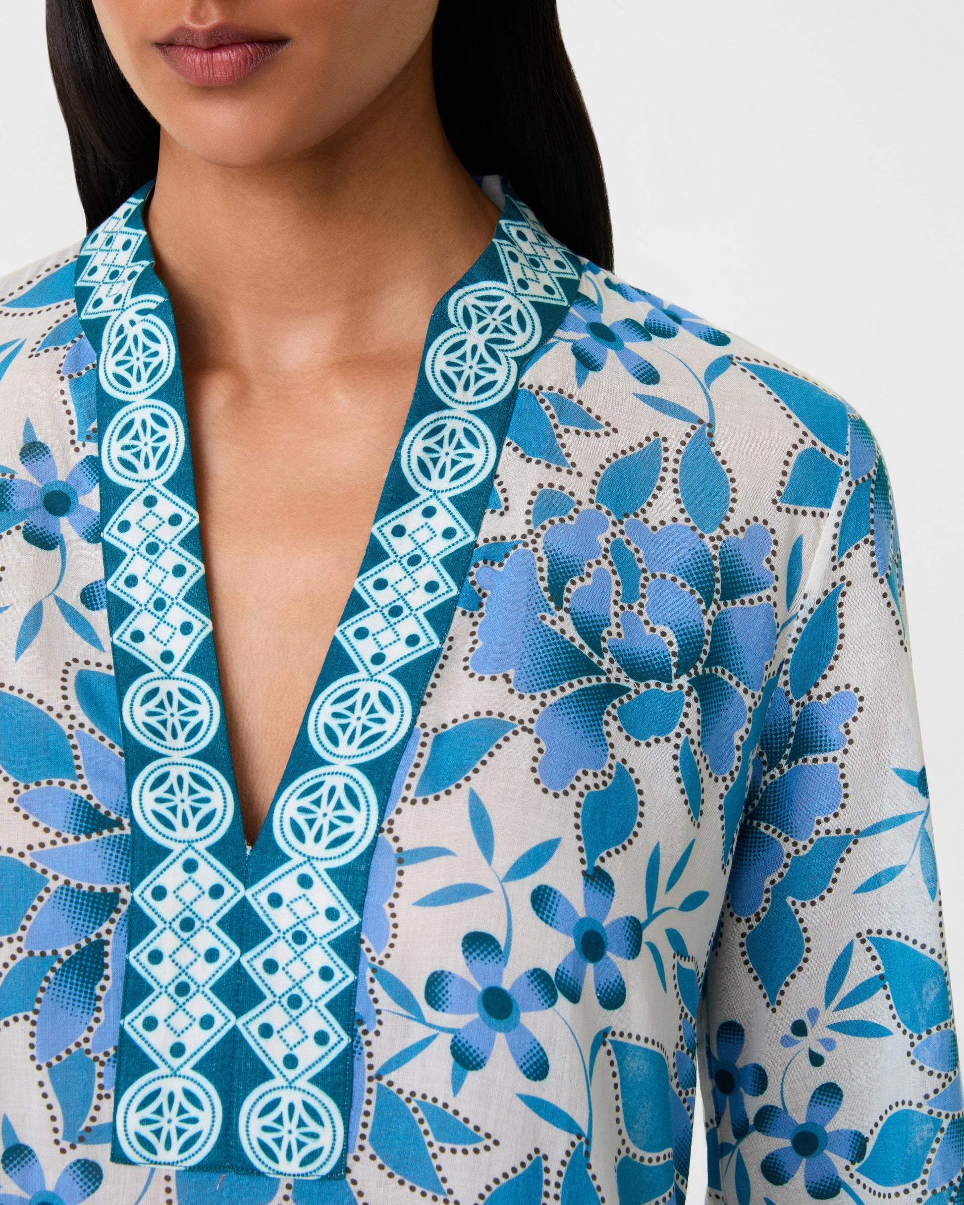 A woman wears the Emporio Sirenuse Jenna Eastern Dream Dress, crafted in soft cotton voile with a blue and white print and geometric embroidery along the neckline.