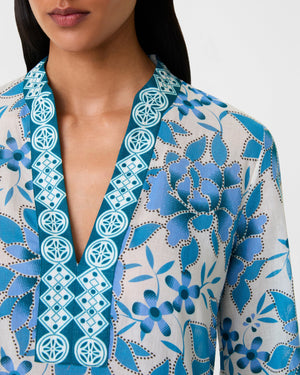 A woman wears the Emporio Sirenuse Jenna Eastern Dream Dress, crafted in soft cotton voile with a blue and white print and geometric embroidery along the neckline.