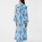 A person stands facing away, wearing the ankle-length Jenna Eastern Dream Dress by Emporio Sirenuse in airy cotton voile, paired with blue sandals.