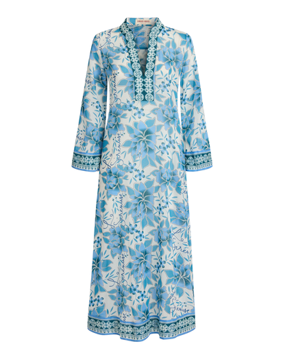 The Emporio Sirenuse Jenna Eastern Dream Dress is a long-sleeve, ankle-length cotton voile caftan with a blue print and decorative trim on the neckline, cuffs, and hem, shown against a white background.