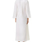 A woman stands facing away, wearing the Jenna Meridiana Dress by Emporio Sirenuse—an ankle-length, long-sleeved white dress with Meridiana embroidery and a loose, graceful fit.