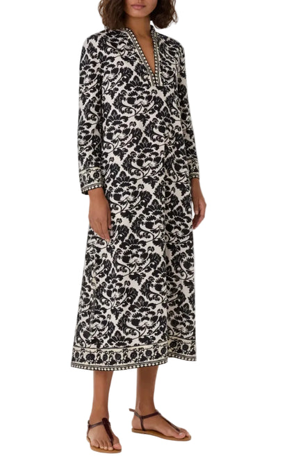 A person wearing a calf-length Emporio Sirenuse Giada Lotus Flower Dress in cotton voile with a black and white floral pattern and a V-neckline.