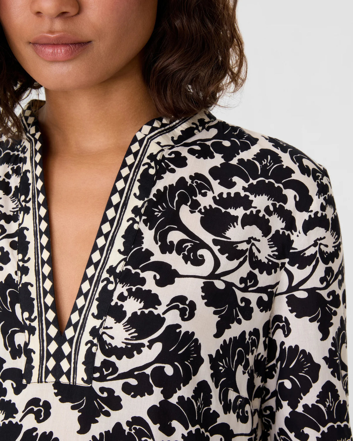 Close-up of an Emporio Sirenuse Giada Lotus Flower Dress in a black and cream print, featuring a V-neckline and geometric diamond-print trim.