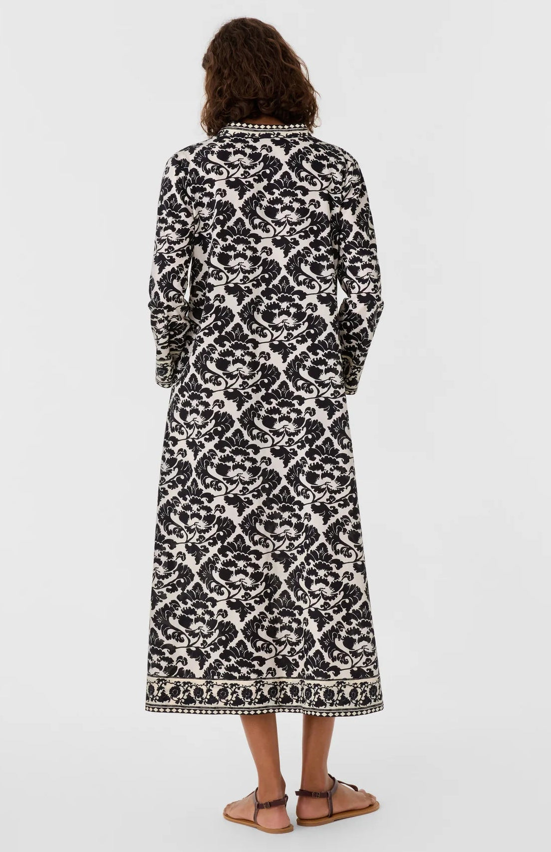 Back view of a person wearing a black and white lotus flower print Giada Lotus Flower Dress, featuring long sleeves and decorative trim at the neckline and hem.