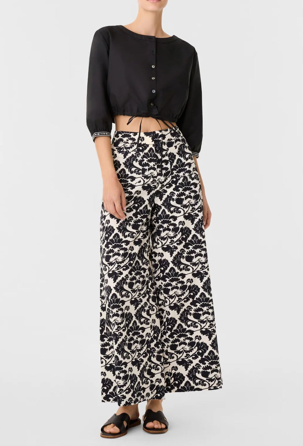 A model wearing a black cropped button-up shirt and Emporio Sirenuse Adele Lotus Flower Pants.