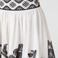 White Ombretta Peony Embroidery Skirt with a gathered silhouette, black patterned waistband, and peony embroidery along the hem.