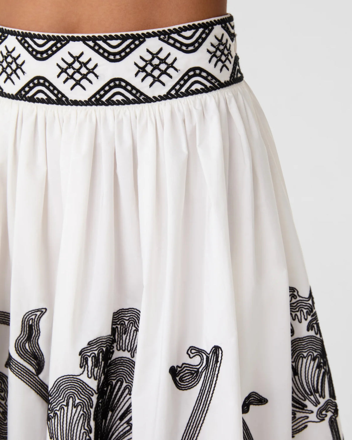 White Ombretta Peony Embroidery Skirt with a gathered silhouette, black patterned waistband, and peony embroidery along the hem.