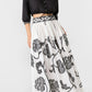 A person wears a black cropped button-up shirt and an Emporio Sirenuse Ombretta Peony Embroidery Skirt in white cotton poplin with black peony embroidery and a patterned waistband.