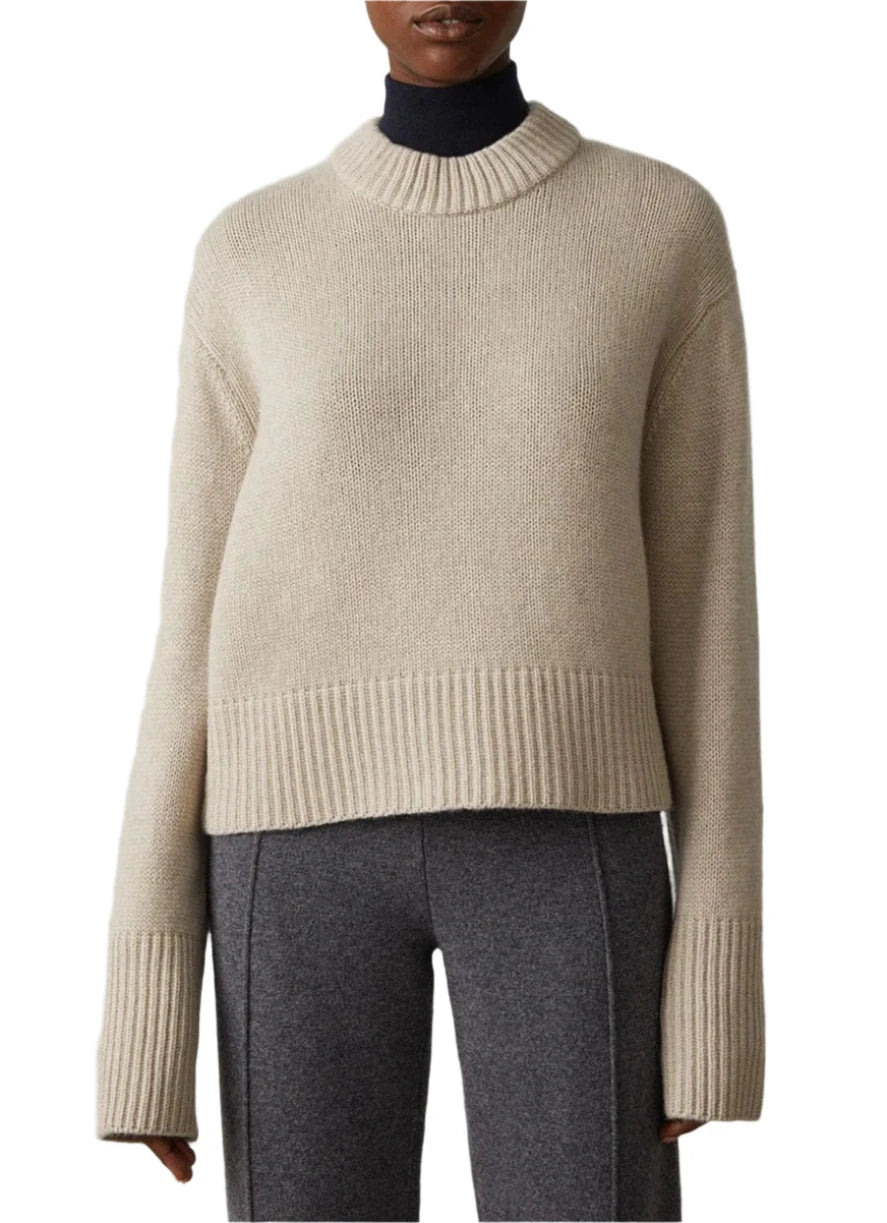 The person is wearing Lisa Yang's Sony Cashmere Sweater in beige, featuring fisherman ribbed trims, paired with grey trousers.