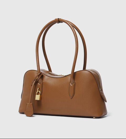 The Ryder Shoulder Bag by Stella McCartney is a brown, cruelty-free handbag with dual handles, a gold padlock detail, and a structured silhouette, shown on a plain light background.