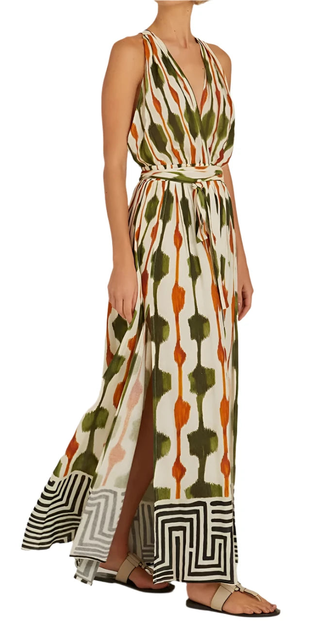 A person wears the Lenny Niemeyer Tie Waist Strap Dress, a sleeveless, floor-length piece featuring a Tanzania print with geometric stripes in green, orange, and white. They finish the ensemble with flat sandals.