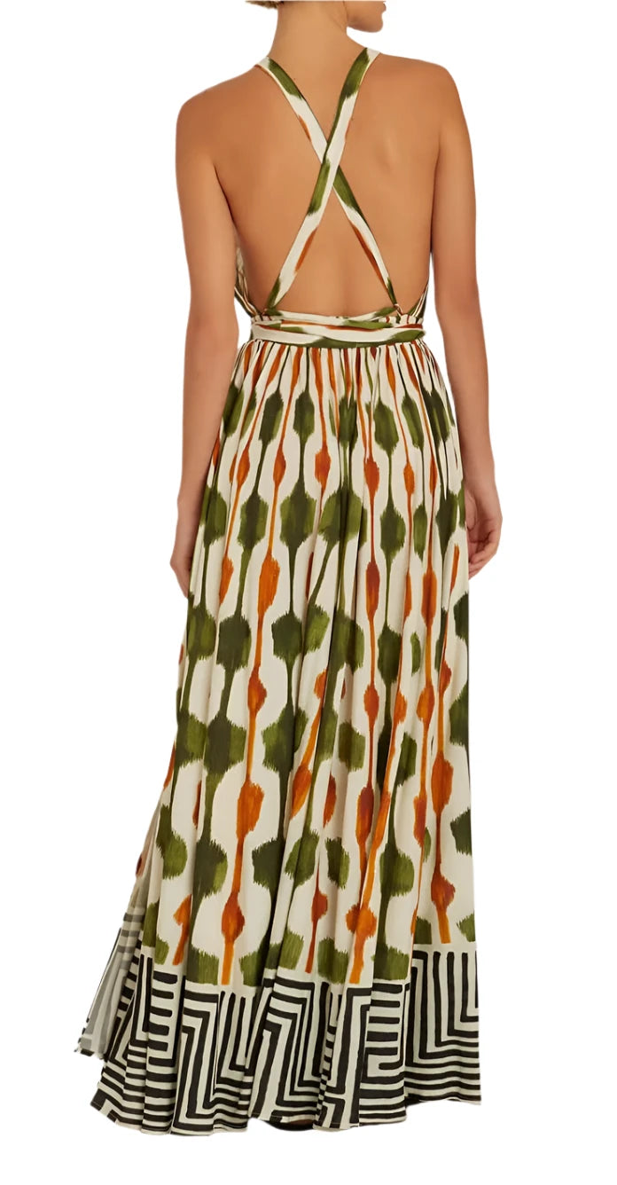 A person is elegantly dressed in the Lenny Niemeyer Tie Waist Strap Dress, a stunning piece featuring a backless, halter-neck design with an orange and green abstract pattern and a geometric stripe border reminiscent of a Tanzania print. The tie waist strap completes their stylish look as they stand with their back to the camera.