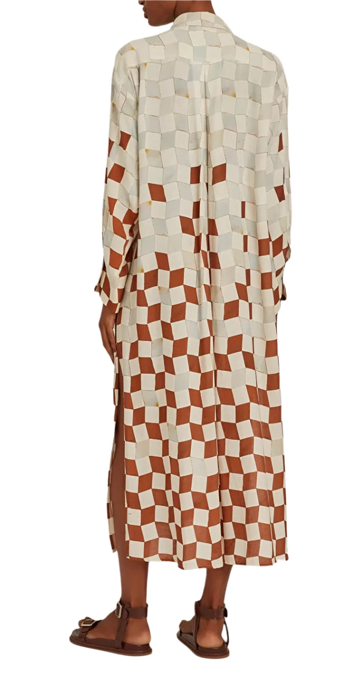 A person stands facing away, showcasing the Lenny Niemeyer Comfort Button Up Shirt Dress featuring a striking casablanca print filled with geometric designs. Sandals peek out beneath the hem, completing the elegantly relaxed look.