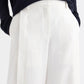 A person wearing a navy long-sleeve top tucked into the TWP Taite Chintzed Linen Pant—a pair of high-rise, wide-leg ivory trousers—with hands in pockets.