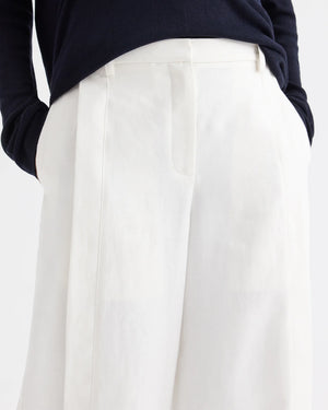 A person wearing a navy long-sleeve top tucked into the TWP Taite Chintzed Linen Pant—a pair of high-rise, wide-leg ivory trousers—with hands in pockets.