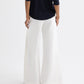 A person stands with their back to the camera, wearing a navy long-sleeve top and TWP’s Taite Chintzed Linen Pant—high-rise, wide-leg ivory pants—against a plain background.