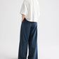 A person stands with hands in pockets, facing away from the camera against a plain white background, wearing a loose white top and the TWP Next Didi Raw Hem Pant — wide-leg, mid-rise navy blue cotton poplin pants.